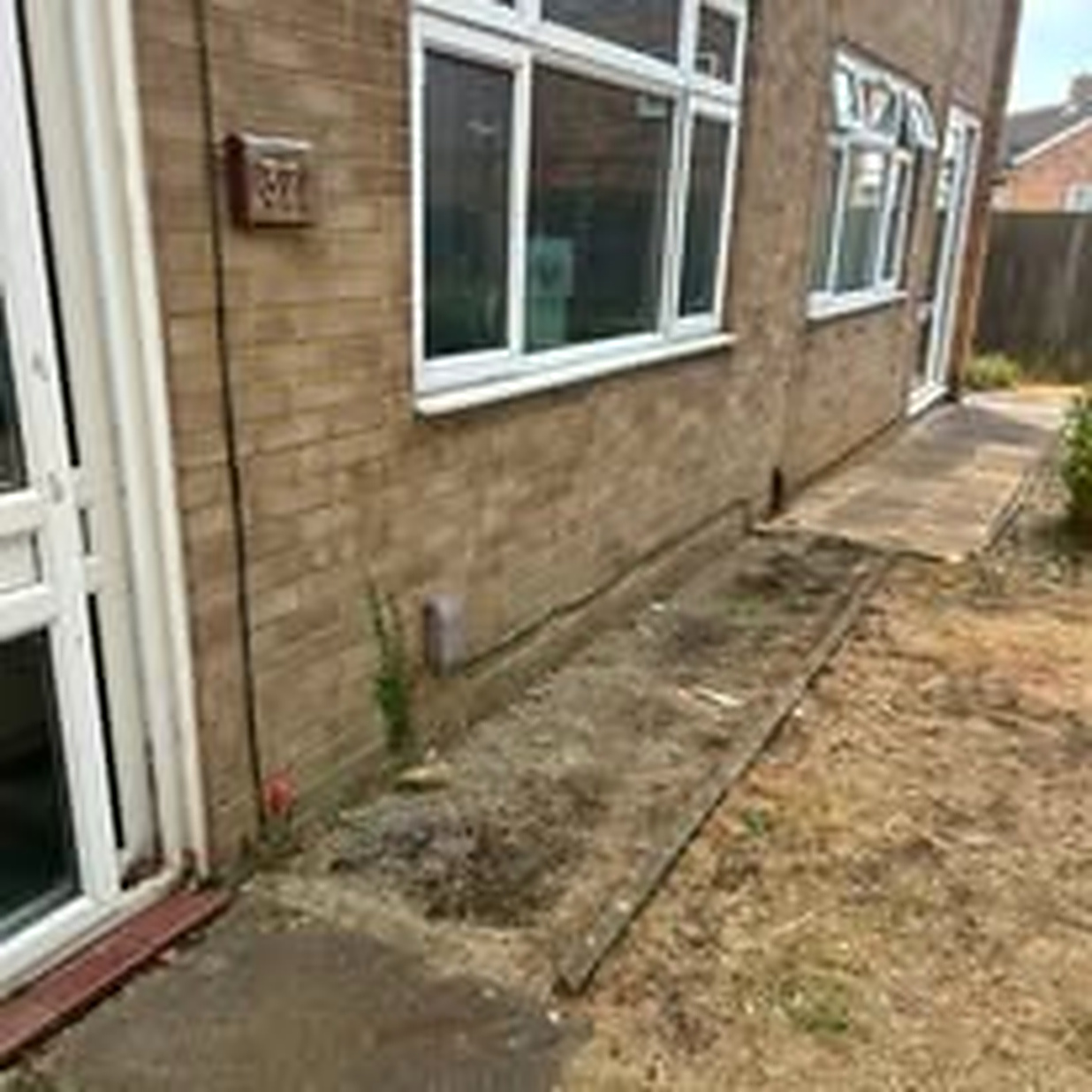 Cleared side of a brick bungalow with a tidy pathway after property clearance