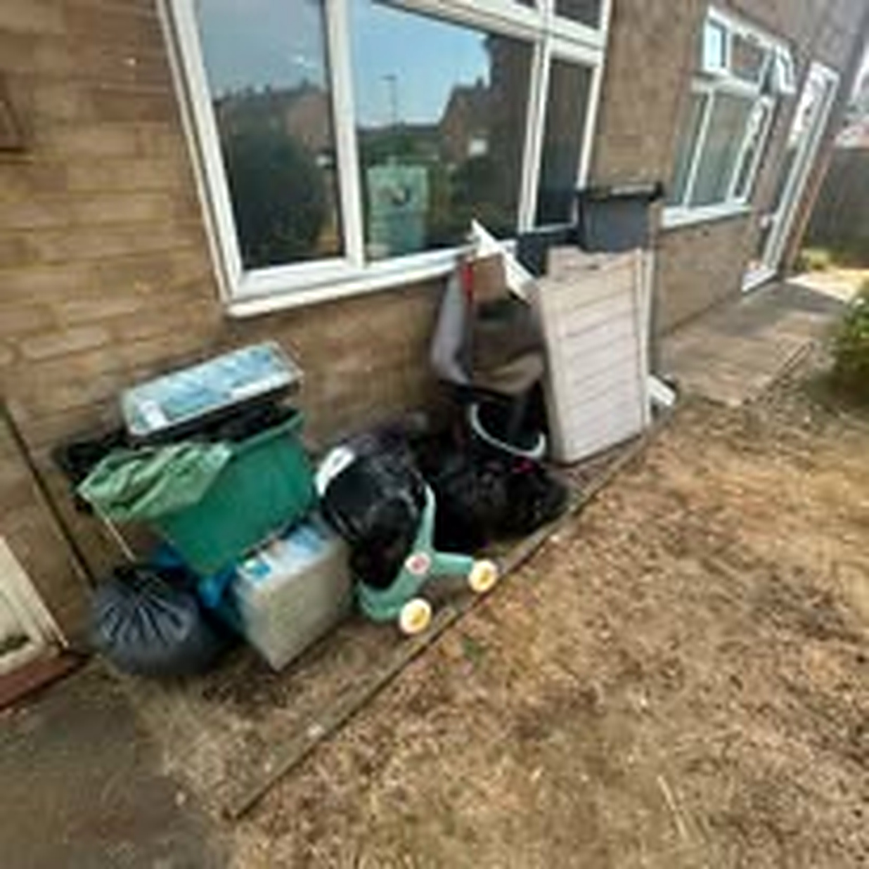 Bin bags, a white furniture unit and garden waste stacked against a brick house wall